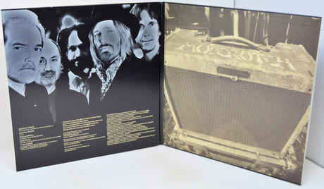 An open vinyl record sleeve or booklet showing printed cover art: a black-and-white band portrait on the left panel and a sepia-toned photo of a Moogith amplifier on the right panel, photographed against a light neutral background.