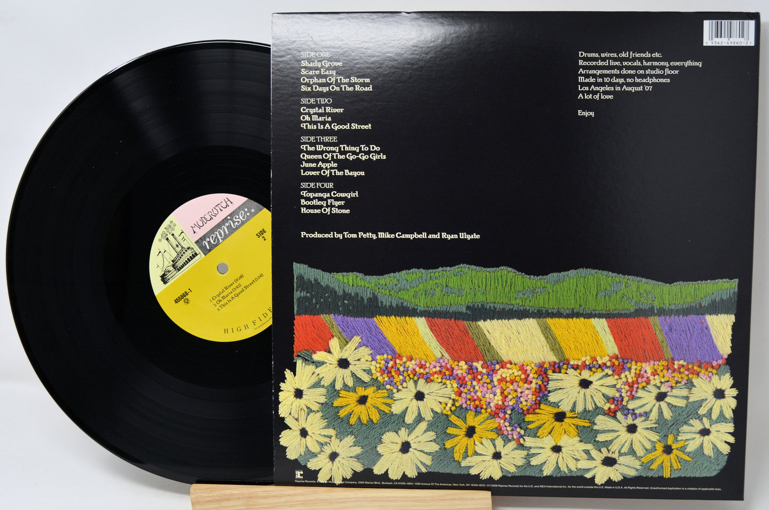 A vinyl record partially pulled from its black album jacket, which features a colorful illustrated landscape of flowers and hills. The record label reads Reprise Records.