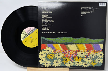 A vinyl record partially pulled from its black album jacket, which features a colorful illustrated landscape of flowers and hills. The record label reads Reprise Records.
