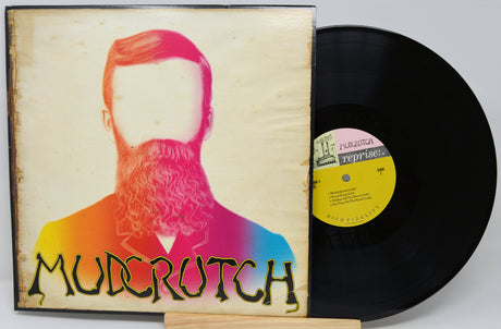 A vinyl record and its album cover for Mudcrutch's 'Reprise' are displayed on a small wooden stand against a light gray background.