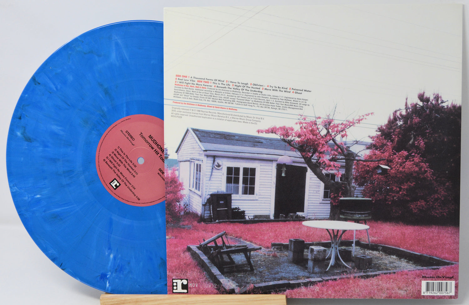 A vinyl record partially visible behind its printed back cover, photographed on a light background. The record is bright translucent blue with a pink center label.