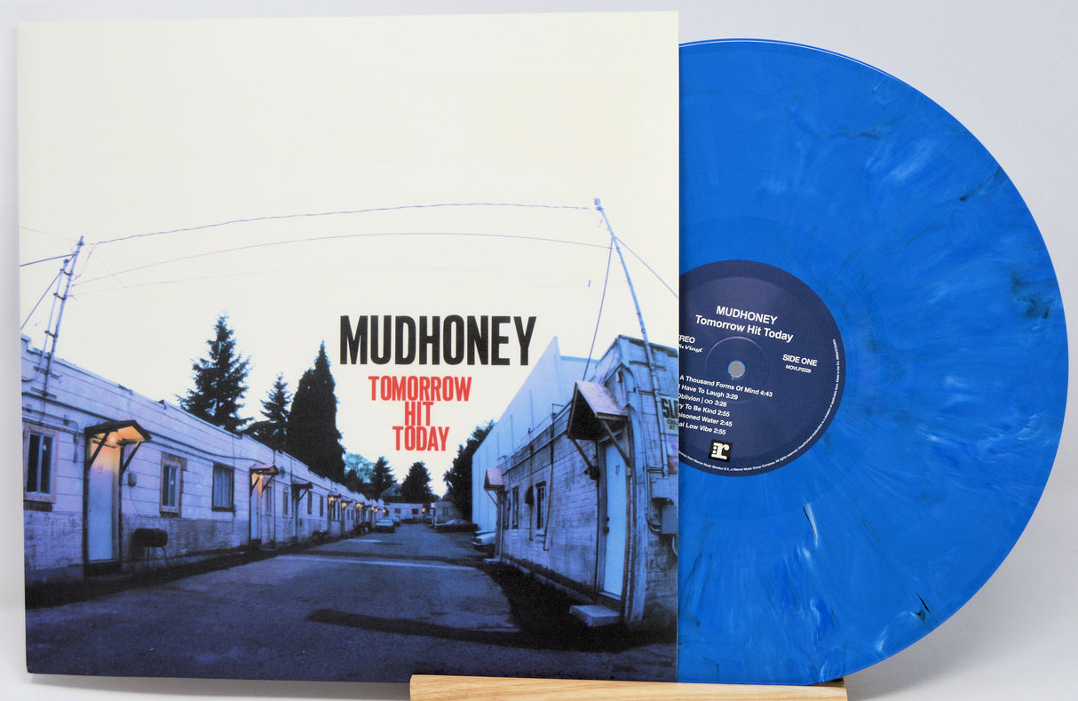 Mudhoney 'Tomorrow Hit Today' vinyl record album with the cover sleeve on the left and a translucent blue marbled record partially visible on the right, displayed on a small wooden stand against a light gray background.