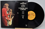 Vinyl record album 'Carnegie Hall Concert Volume 1' by Gerry Mulligan and Chet Baker, showing the black cover with a performer photo and the black record partially pulled out, displayed on a stand against a light gray background.