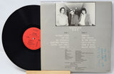 Vinyl record with cover featuring a black and white photo of three people and text.