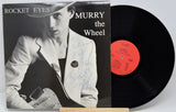 Vinyl record with cover featuring a person holding a guitar, titled 'Rocket Eyes Murry the Wheel'.