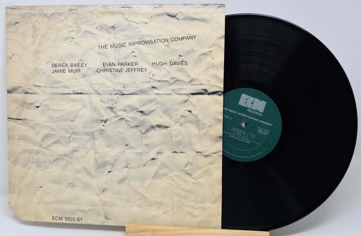A vintage ECM 1005 ST vinyl record partially pulled from its worn paper sleeve. The sleeve is cream/beige with black printed text listing the music improvisation company and cast names, while the black vinyl disc shows a green ECM label.