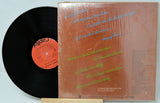 Vinyl record with a brown cover featuring text and a red label on a light gray background