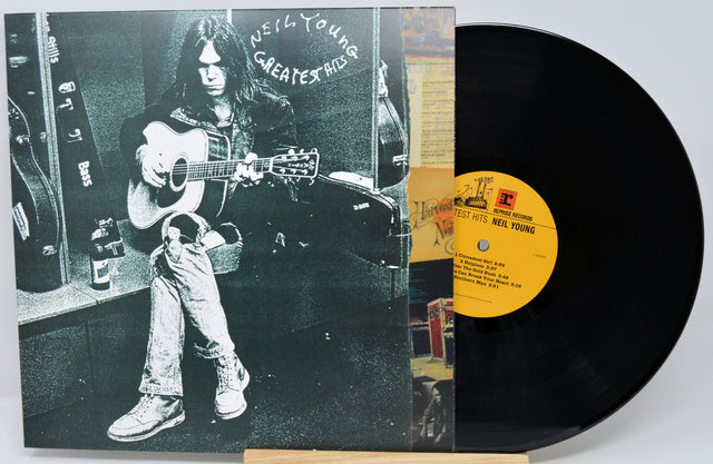 Neil Young's 'Greatest Hits' vinyl record album, showing the black-and-white cover jacket on the left and the black LP record partially pulled out on the right with a yellow label.