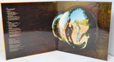 An open vinyl record sleeve or album booklet showing printed track listings on the left page and a large reflective circular mirror graphic on the right, with a person reflected in the mirror.
