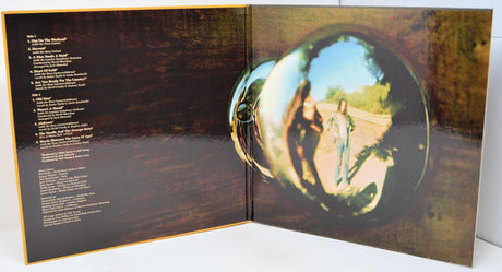 An open vinyl record sleeve or album booklet showing printed track listings on the left page and a large reflective circular mirror graphic on the right, with a person reflected in the mirror.