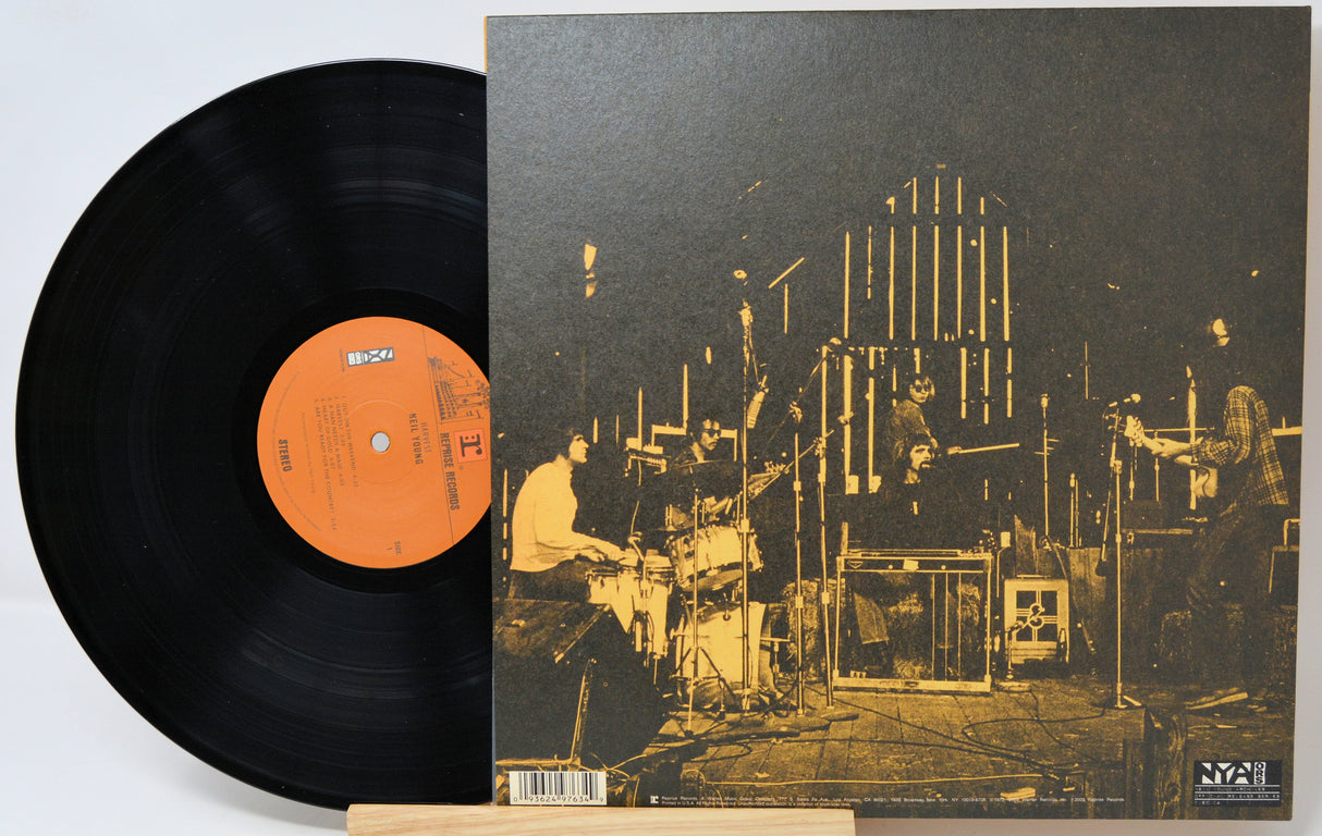 A vinyl record partially pulled from its sleeve, showing the black record with an orange center label and the album cover featuring a sepia-toned concert scene.