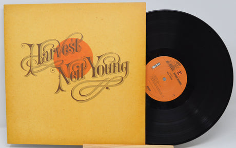 Neil Young's 'Harvest' vinyl record album, showing the mustard-yellow sleeve with stylized lettering and an orange sun graphic, next to the black LP record with an orange center label.