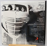The back cover of a Misson sings Newman vinyl record album, showing black and white artwork of a vintage car with band members in the window, track listings, and a small photo of the record label, Republic, resting on a wooden surface.