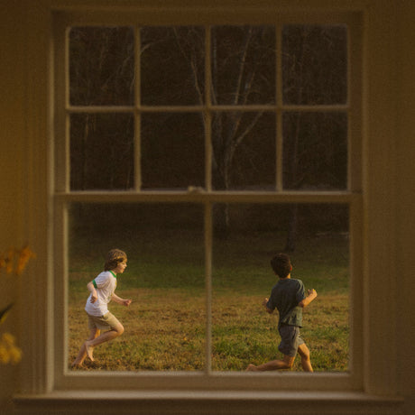 Two children running in a field as seen through a window.