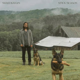 Noah Kahan 'Stick Season' vinyl album cover showing him standing in a field with two dogs, with a barn and trees in the background. He is wearing a grey jacket and black pants.