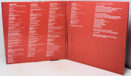 An open vinyl record sleeve or booklet showing the back cover with dense white track listings and text on a red background, photographed on a white surface.
