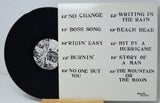 Vinyl record with white label displaying tracklist on a light gray background