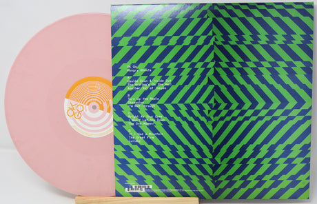 Vinyl record with a pink disc and a green and blue geometric patterned cover.