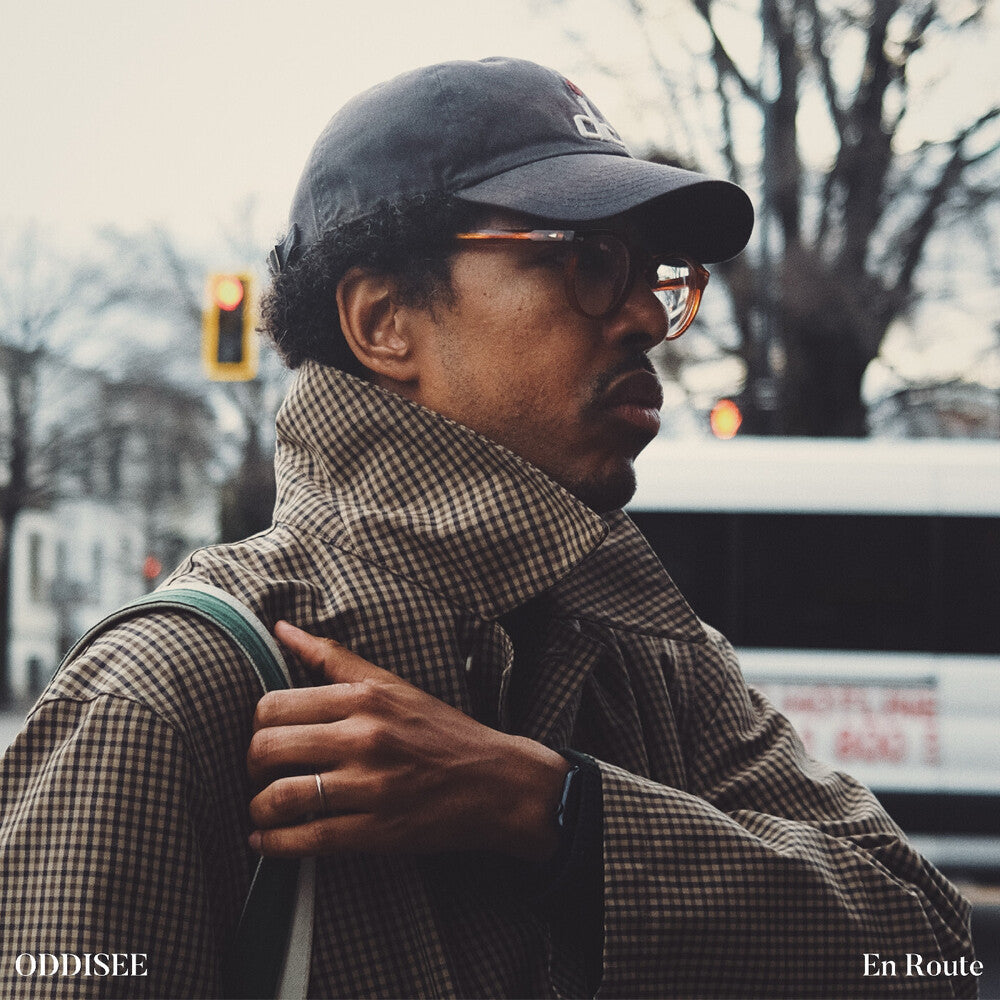 Man wearing a cap, glasses, and plaid scarf on a city street.