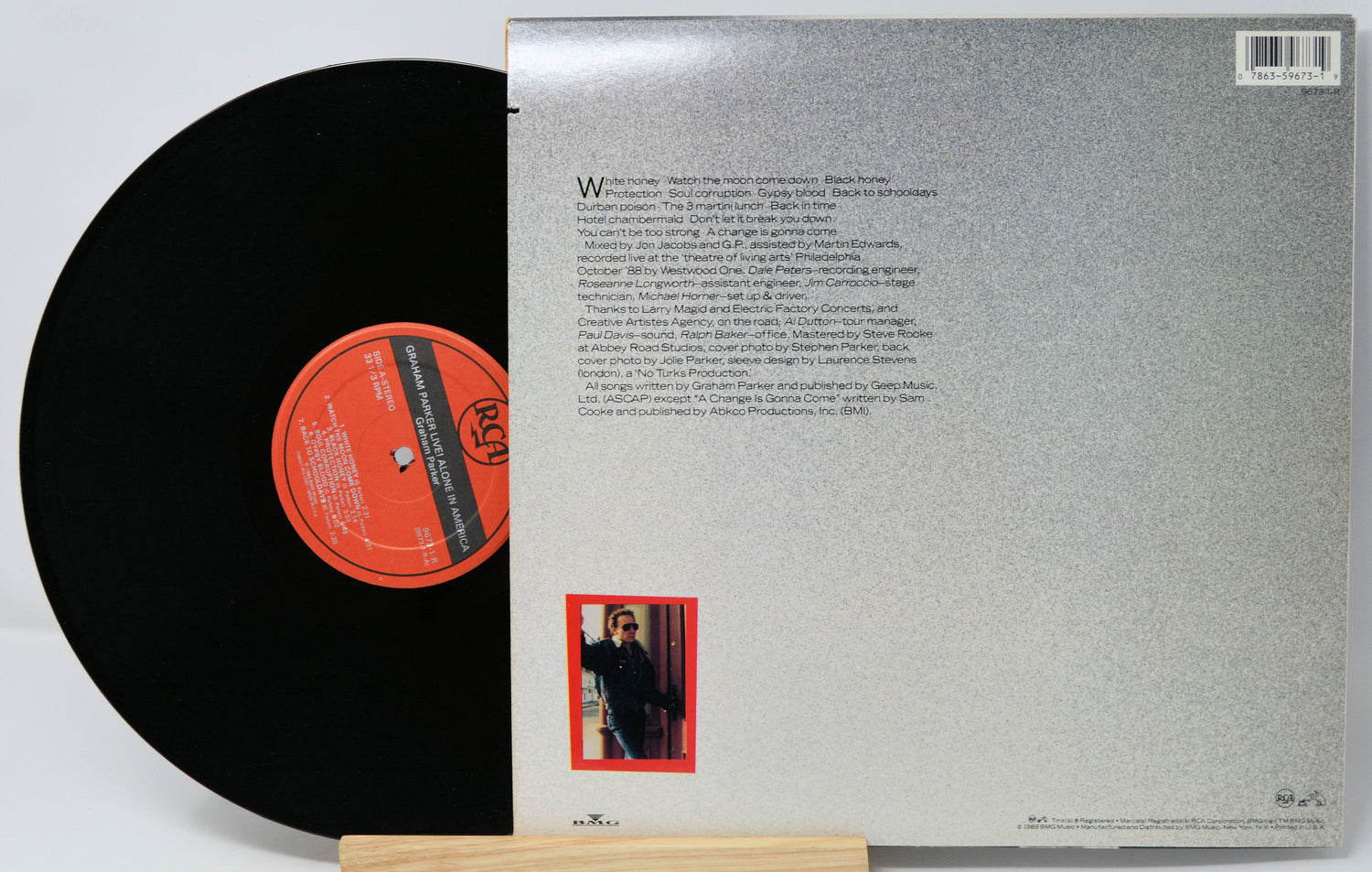 Vinyl record with black disc and red label, standing next to its gray cover with text.