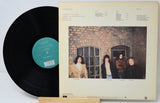 Vinyl record with a cover featuring four people in front of a brick wall.