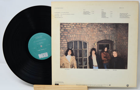 Vinyl record with a cover featuring four people in front of a brick wall.