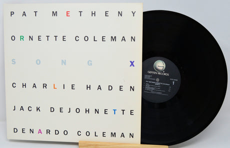 Vinyl record with cover featuring artist names on a light gray background