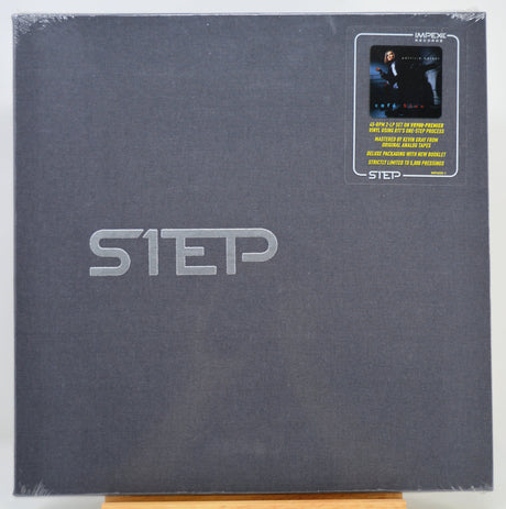 A square dark gray album or book-style package with large embossed 'STEP' lettering and a small 'IMPEX' sticker in the top-right corner, photographed against a plain light background.
