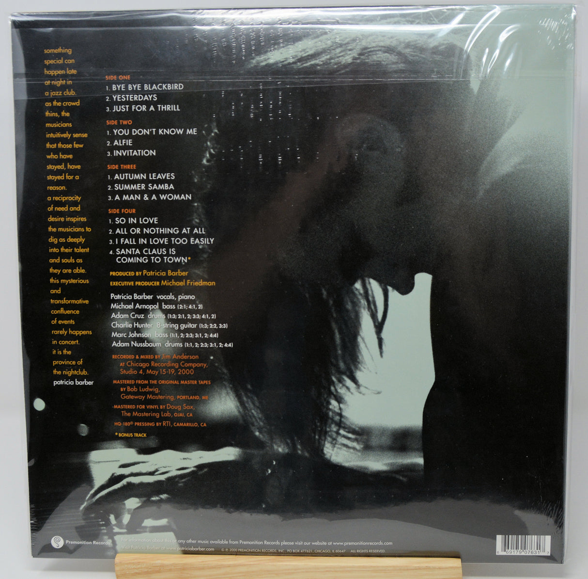 The back cover of a vinyl record album in its shrink wrap, featuring a large black-and-white silhouette of a woman's profile with the tracklist printed in yellow and orange text on a dark background.