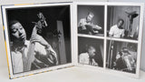 An open printed album or photo book showing black-and-white photographs of a musician playing instruments, including a large bass portrait on the left page and four smaller monochrome photos on the right.