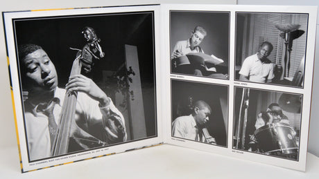 An open printed album or photo book showing black-and-white photographs of a musician playing instruments, including a large bass portrait on the left page and four smaller monochrome photos on the right.