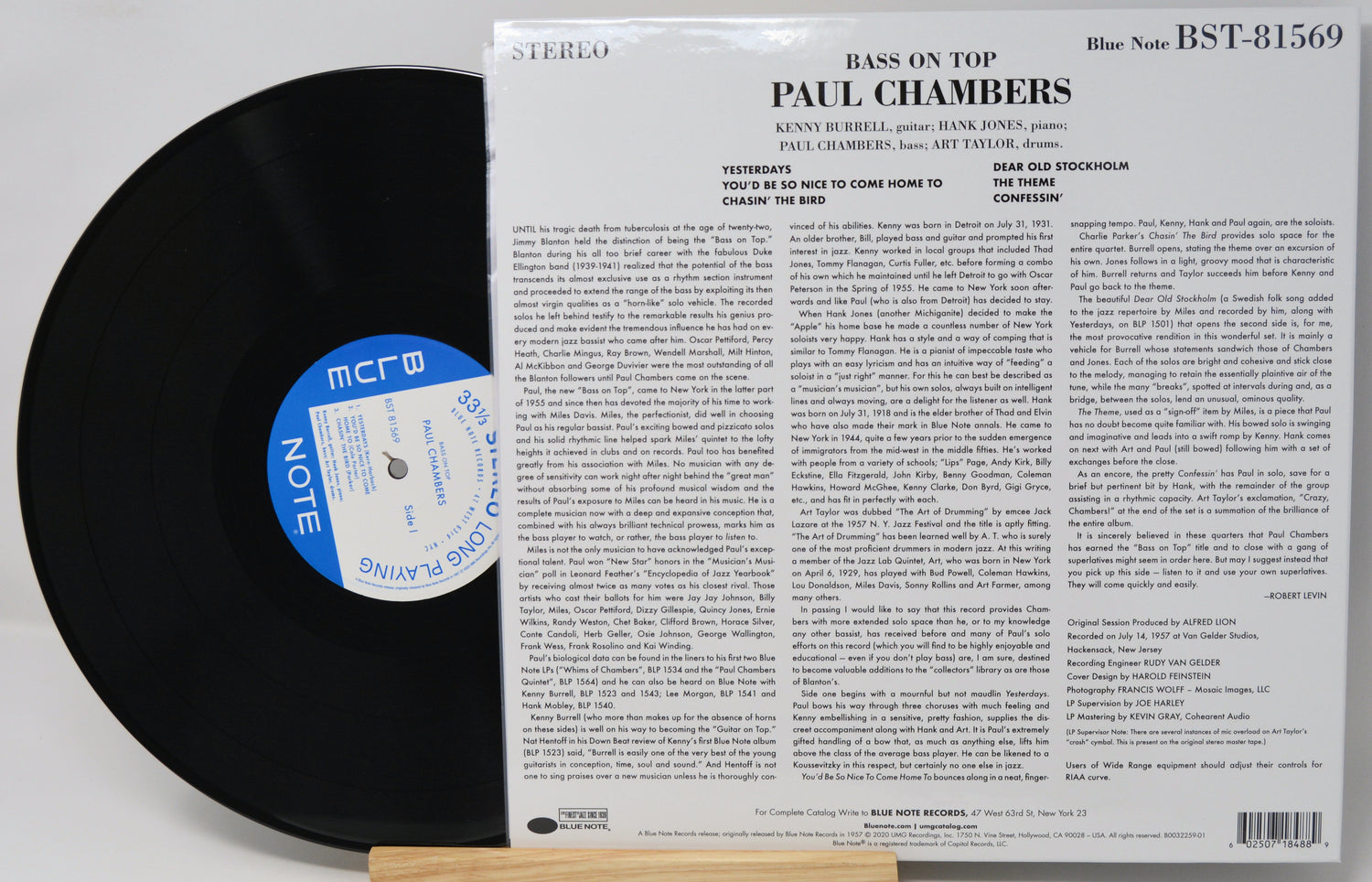 A vinyl record partially pulled from its back cover sleeve, showing the black record with a blue-and-white center label next to the printed album insert for Paul Chambers' 'Bass on Top'.