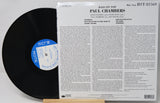 A vinyl record partially pulled from its back cover sleeve, showing the black record with a blue-and-white center label next to the printed album insert for Paul Chambers' 'Bass on Top'.