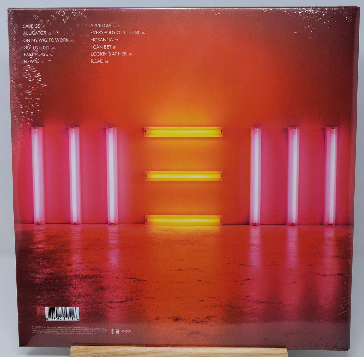 Vinyl record album cover for 'All Is Lost' on a wooden display stand, showing a reflective orange and red floor with pink and yellow vertical light tubes.