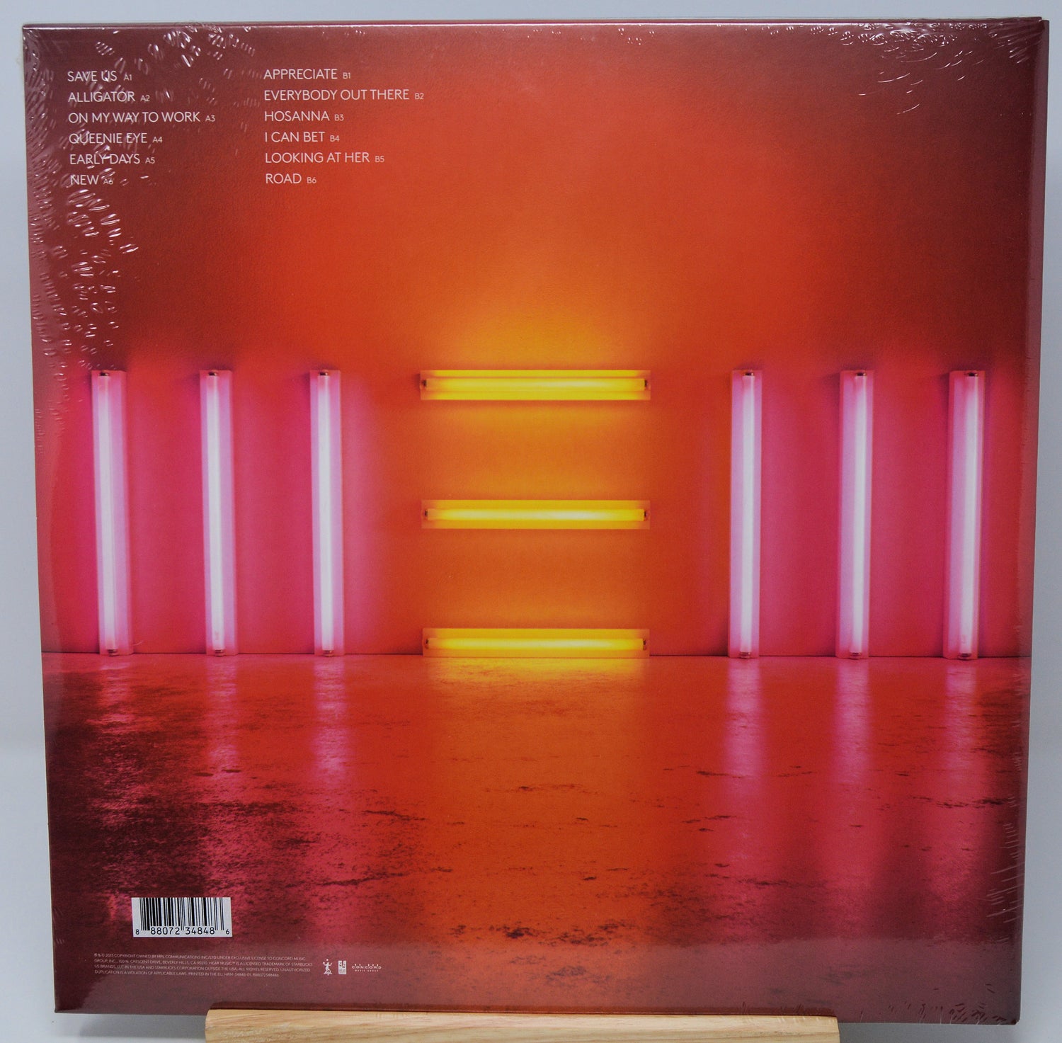 Vinyl record album cover for 'All Is Lost' on a wooden display stand, showing a reflective orange and red floor with pink and yellow vertical light tubes.