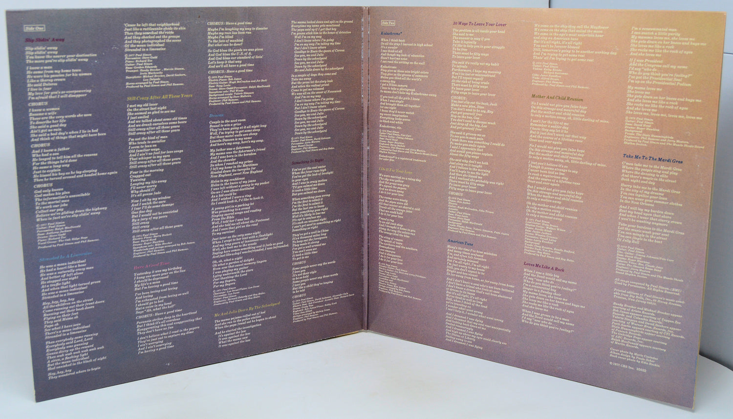An open booklet or album insert with dense columns of small text printed in white and purple on a purple-to-peach gradient background, photographed against a plain light surface.