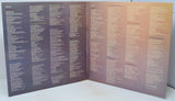 An open booklet or album insert with dense columns of small text printed in white and purple on a purple-to-peach gradient background, photographed against a plain light surface.