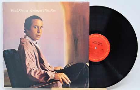 Vinyl record album for Paul Simon's 'Greatest Hits, Etc.' with the album cover standing on the left and the black LP record partially pulled out on the right, photographed against a plain light background.