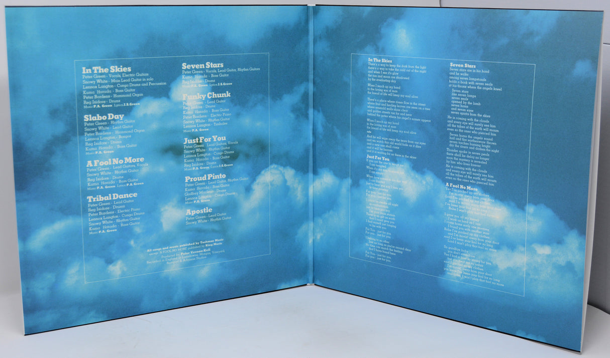 An open vinyl record sleeve or booklet printed with a blue sky and clouds background, displaying song titles in white text on both inner pages.