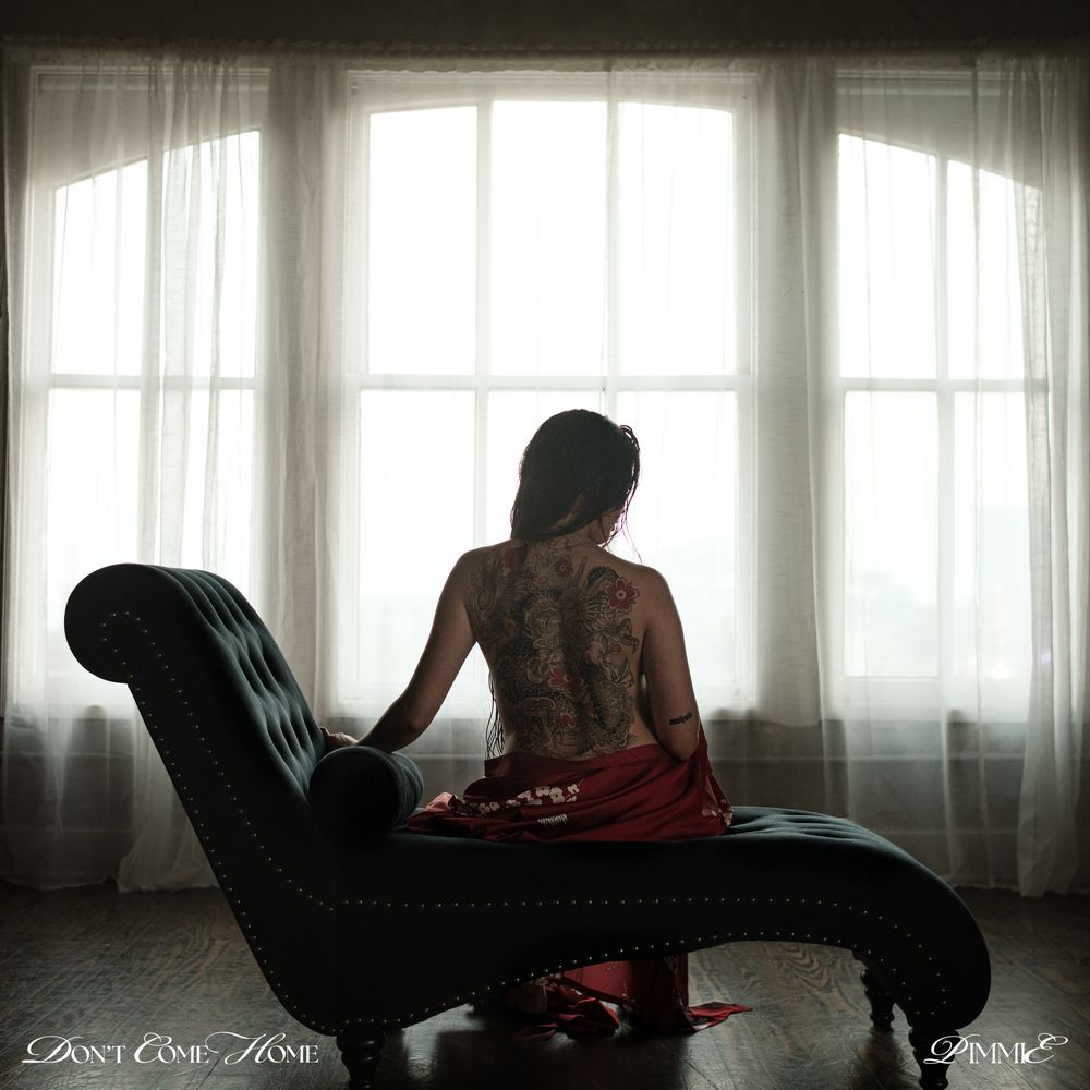 Woman sitting on a chaise lounge in front of large windows with sheer curtains.