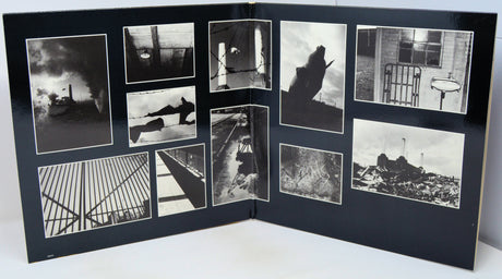 An open black photo album or book spread, displaying multiple black-and-white photographic prints arranged in a collage layout on the interior pages.