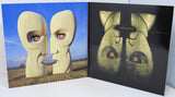 A vinyl record sleeve shown open, displaying the front cover artwork on the left and the inner sleeve artwork on the right. The surreal artwork features two large beige stone-like faces facing each other under a blue sky, with a field at the bottom and a black background on the inner sleeve.
