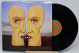 Vinyl record partially pulled from its sleeve, showing the album cover artwork of two large wooden faces facing each other with a UFO between them, and the black record with a green and red center label.