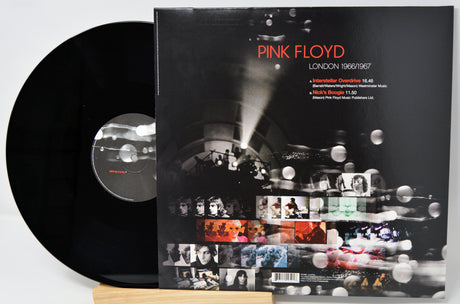 Pink Floyd 'London 1969/1977' vinyl record shown with the black LP disc partially pulled from the sleeve, photographed on a light gray background with a small wooden stand.