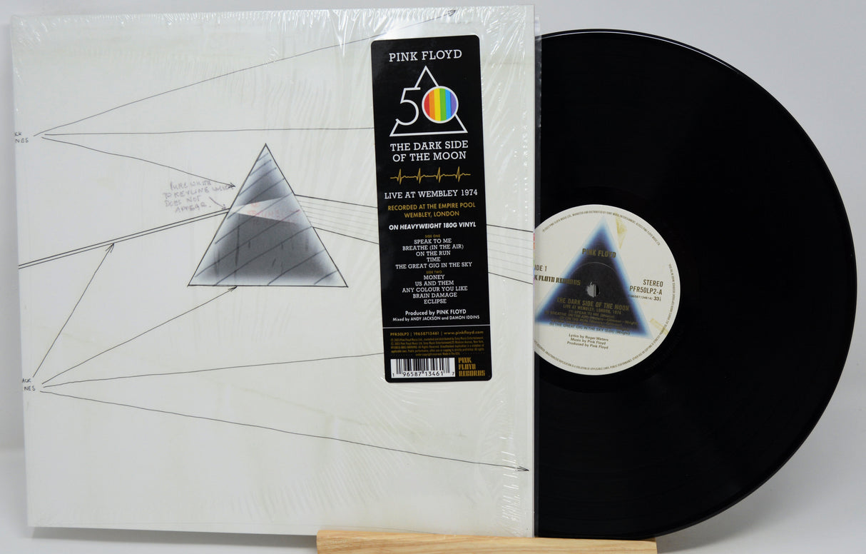 Pink Floyd 'The Dark Side of the Moon' 12-inch vinyl record shown in its shrink-wrapped outer sleeve with the black LP record partially pulled out, displayed on a small wooden stand against a light gray background.