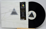 Pink Floyd 'The Dark Side of the Moon' 12-inch vinyl record shown in its shrink-wrapped outer sleeve with the black LP record partially pulled out, displayed on a small wooden stand against a light gray background.