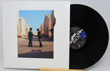 A vinyl record partially pulled from its white sleeve, showing the album cover art with a photo of two men shaking hands outdoors, alongside the black record with a blue and white label.