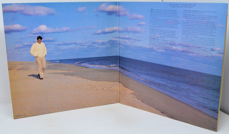 Open book showing a person walking on a beach with a blue sky.