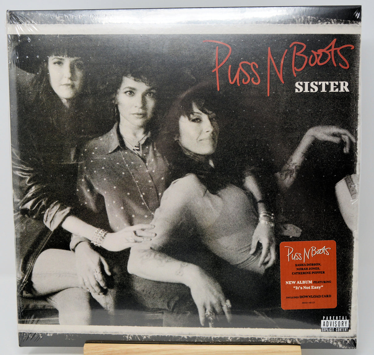 Puss N Boots - Sister vinyl record album cover, showing a black and white photo of three women with red and white title text, plus an orange sticker on the lower right.