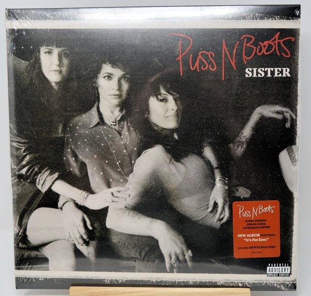 Puss N Boots - Sister vinyl record album cover, showing a black and white photo of three women with red and white title text, plus an orange sticker on the lower right.